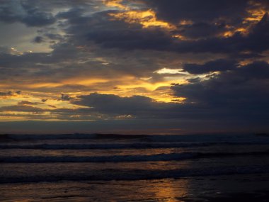Okyanus dalgaları ön planda ile bulutlu gün batımı