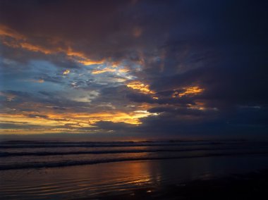 Okyanus dalgaları ön planda ile bulutlu gün batımı
