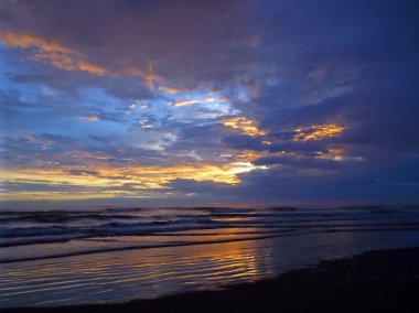 Okyanus dalgaları ön planda ile bulutlu gün batımı