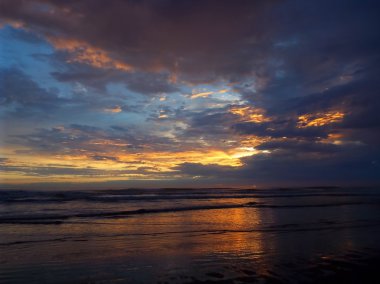 Okyanus dalgaları ön planda ile bulutlu gün batımı