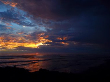 Okyanus dalgaları ön planda ile bulutlu gün batımı