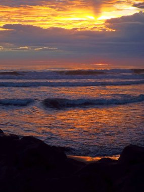 Okyanus dalgaları ön planda ile bulutlu gün batımı