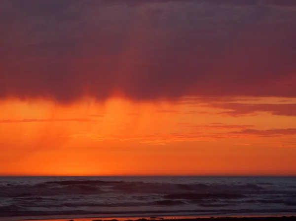 Zataženo západ slunce nad oceánem s vlnami v popředí — Stock fotografie