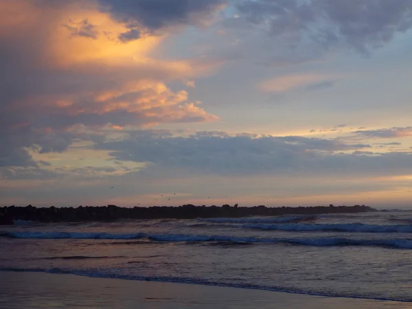 Pôr-do-sol nublado sobre o oceano com ondas em primeiro plano — Fotografia de Stock