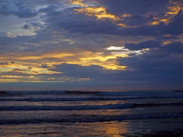 Bewolkt zonsondergang Over de oceaan met golven op de voorgrond — Stockfoto