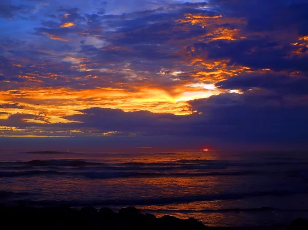 Wolkenverhangener Sonnenuntergang über dem Meer mit Wellen im Vordergrund — Stockfoto