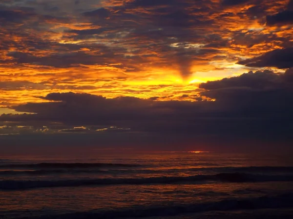 Pôr-do-sol nublado sobre o oceano com ondas em primeiro plano — Fotografia de Stock