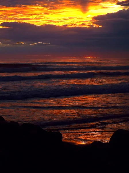 Wolkenverhangener Sonnenuntergang über dem Meer mit Wellen im Vordergrund — Stockfoto