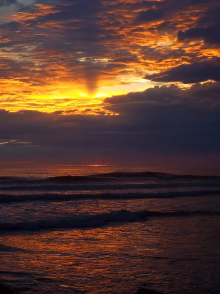 Wolkenverhangener Sonnenuntergang über dem Meer mit Wellen im Vordergrund — Stockfoto