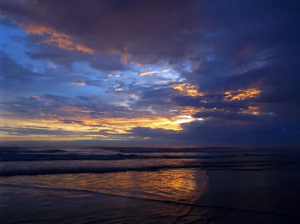 Tramonto nuvoloso sull'oceano con onde in primo piano Fotografia Stock