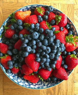 Ahşap bir masa üzerinde bir kasede bir yaban mersini ve çilek