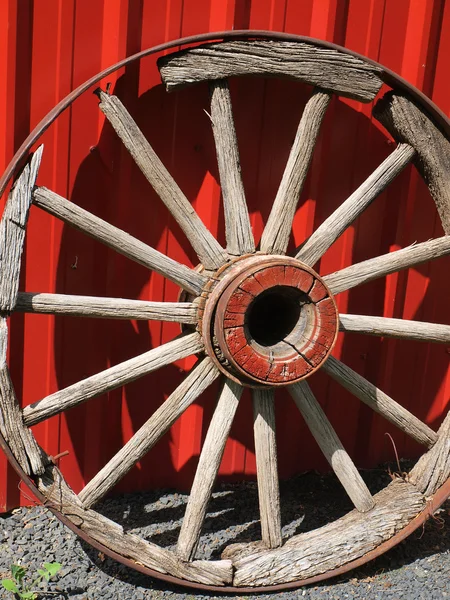 Vecchia ruota del carro di legno appoggiata contro una parete rossa — Foto Stock