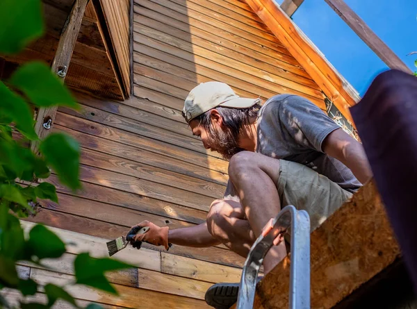 Человек красит деревянную стену дома на открытом воздухе — стоковое фото