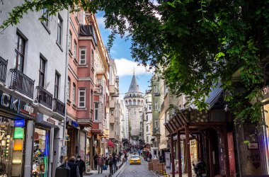 Istanbul, Turkey - November, 11, 2020: Galata Tower and a narrow vintage street with a yellow taxi.