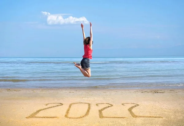 Año Nuevo 2022 en la arena, chica feliz con las manos en alto saltando en la playa —  Fotos de Stock