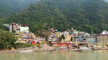 Ganj nehri kıyıları ve Hindistan 'daki yeşil tepeler boyunca renkli binalarla Rishikesh şehrinin panoramik manzarası.