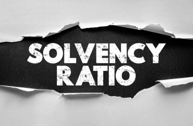Yırtık kağıt üzerinde SOLVENCY RATIO metni. Şirket sağlığı ve iş ve analiz görsellerinde kullanılan uzun vadeli yükümlülükleri yerine getirebilme becerisini gösteren mali istikrar kavramı
