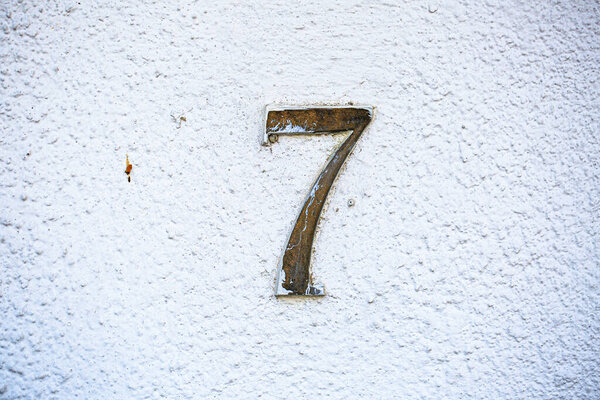 Rustic metal number 7 on a white plaster wall. Minimalist and weathered architectural sign showing texture and simplicity of aged design