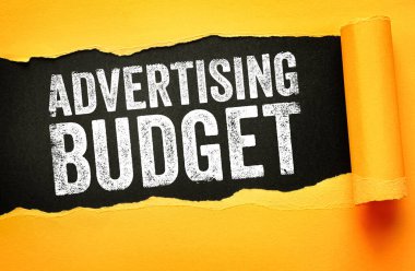 Reklam Bütçesi metni yırtık kağıdın altında görünüyor. Medya kampanyaları ve marka farkındalığı artışı için pazarlama finansmanı, tanıtım planlaması ve iş harcamaları kavramı
