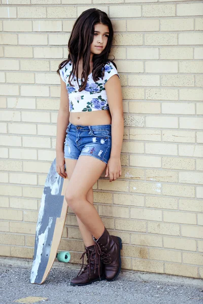 Chica apoyada en la pared de ladrillo con tabla de skate — Foto de Stock