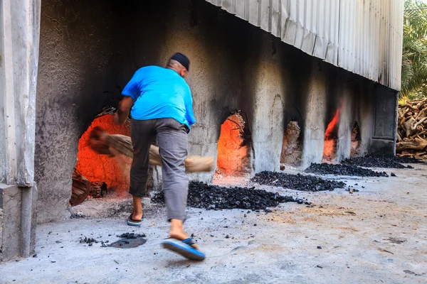 Factory worker is trowing log into oven — Stock Photo, Image