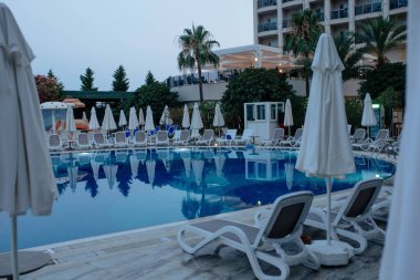 Mavi havuz, şemsiyeler ve otel hindisi güneşlikleri. Beş yıldızlı turizm ve eğlence konsepti