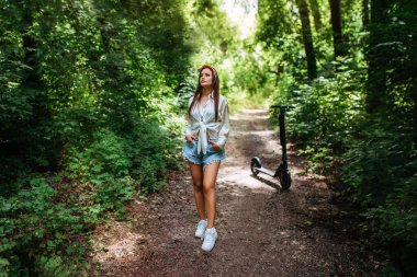 Parkta elektrikli scooter 'a binen tatlı esmer kız beyaz bir gömlek giyiyor. eko taşıma ve kira kavramı. 