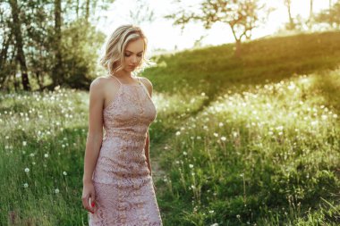 Gün batımında pembe elbiseli bir karahindiba tarlasında bir kadın. Konsept alerjik değil. .