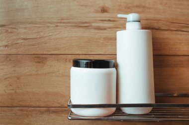 a bottle of shampoo and hair balm sits on a shelf in a bathroom with a wooden wall. concept hair and body care