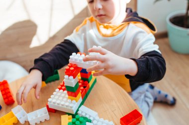 a blond boy is playing with a construction kit, with a wooden wall in the background. close-up