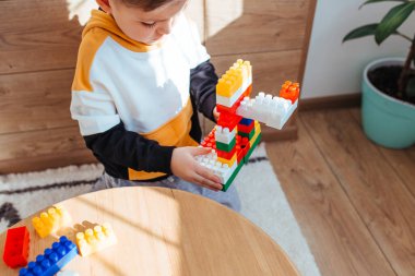 a blond boy is playing with a construction kit, with a wooden wall in the background.