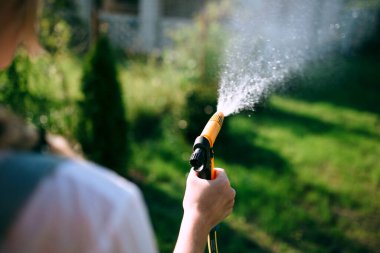 a young woman in a white shirt and denim overalls watering the lawn. gardening concept and landscape design