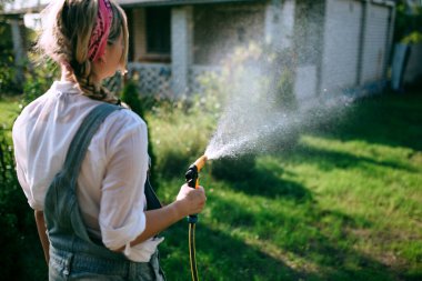 a young woman in a white shirt and denim overalls watering the lawn. gardening concept and landscape design
