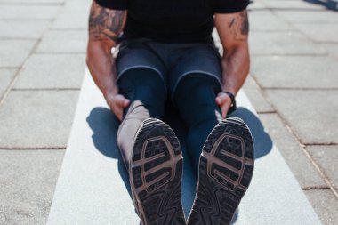 Alıştırma yapmadan önce esneme hareketleri yapan çekici bir genç adam. Gün doğarken de ışık arkadan vuruyor. Sığ alan derinliği, ayakkabılara odaklan