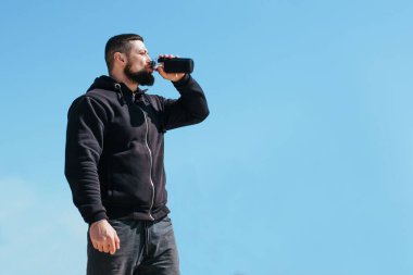 Şişirilmiş sporcu su içer ve kumlu bir dağda koştuktan sonra dinlenir.