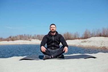 Kum üzerinde antrenmandan sonra kaslı sporcu meditasyon yapar.