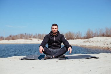 Kum üzerinde antrenmandan sonra kaslı sporcu meditasyon yapar.