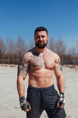 Kaslı boksör çıplak bir gövdeyle kumda çalışır.