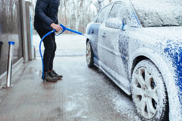 a man with a gun to apply foam on the car. self-service car wash