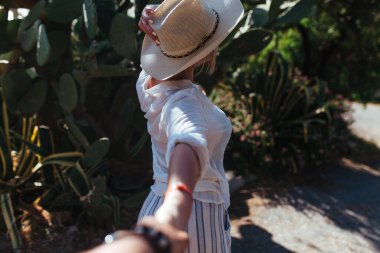 Beyaz gömlekli ve şapkalı bir kadın kaktüsün arka planında duruyor.