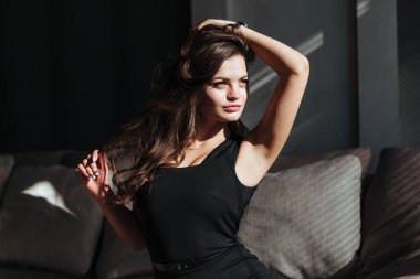 Siyah elbiseli bir kız kanepede oturur ve pencereden dışarı bakar.