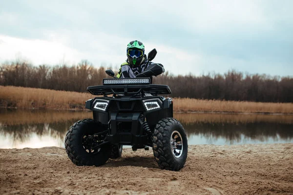 O motorista senta-se em uma moto quad no fundo do rio e areia. desporto e conceito extremo — Fotografia de Stock