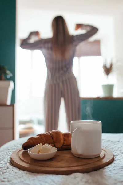 Croissant och kaffe i förgrunden på baksidan av en flicka i pyjamas — Stockfoto