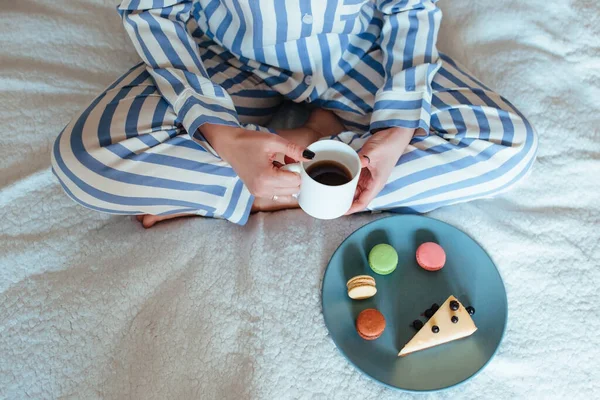 Una mujer por la mañana bebe café y come dulces tarta de queso macarrones dulces —  Fotos de Stock