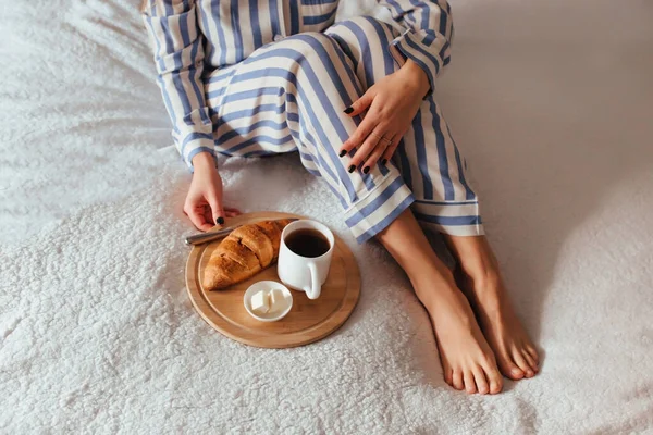 잠옷을 입고 아름다운 다리를 하고 크로 와 상을 입은 커피 옆에 앉는다. 침대에서 커피를 마시는 개념 — 스톡 사진