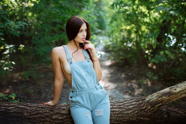 Junge Frau in Jeans-Overalls steht unter Baum im Wald — Stockfoto