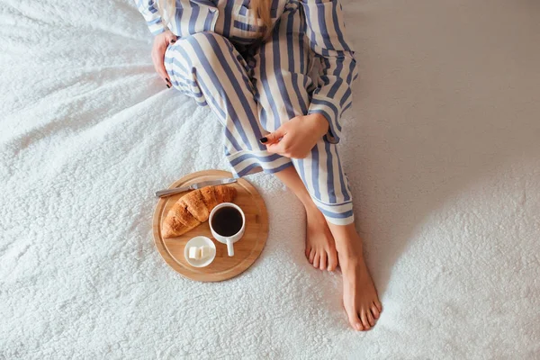 Womens beautiful legs in pyjamas and next to a coffee with a croissant.the concept of coffee in bed — Stock Photo, Image