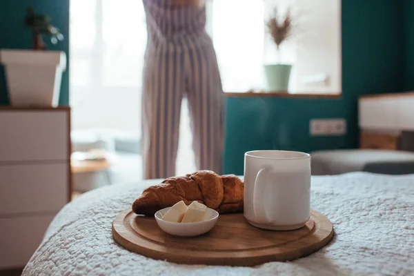 Croissant och kaffe i förgrunden på baksidan av en flicka i pyjamas — Stockfoto