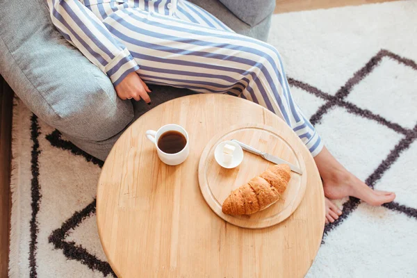Una mujer en pijama por la mañana en una mesa bebe café y come dulces tarta de queso macarrones dulces —  Fotos de Stock