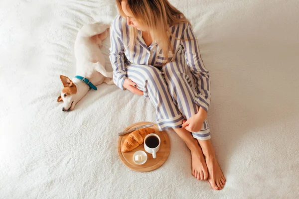 Πρωινό στο κρεβάτι κρουασάν και καφέ. Δίπλα της είναι μια γυναίκα με πιτζάμες. — Φωτογραφία Αρχείου